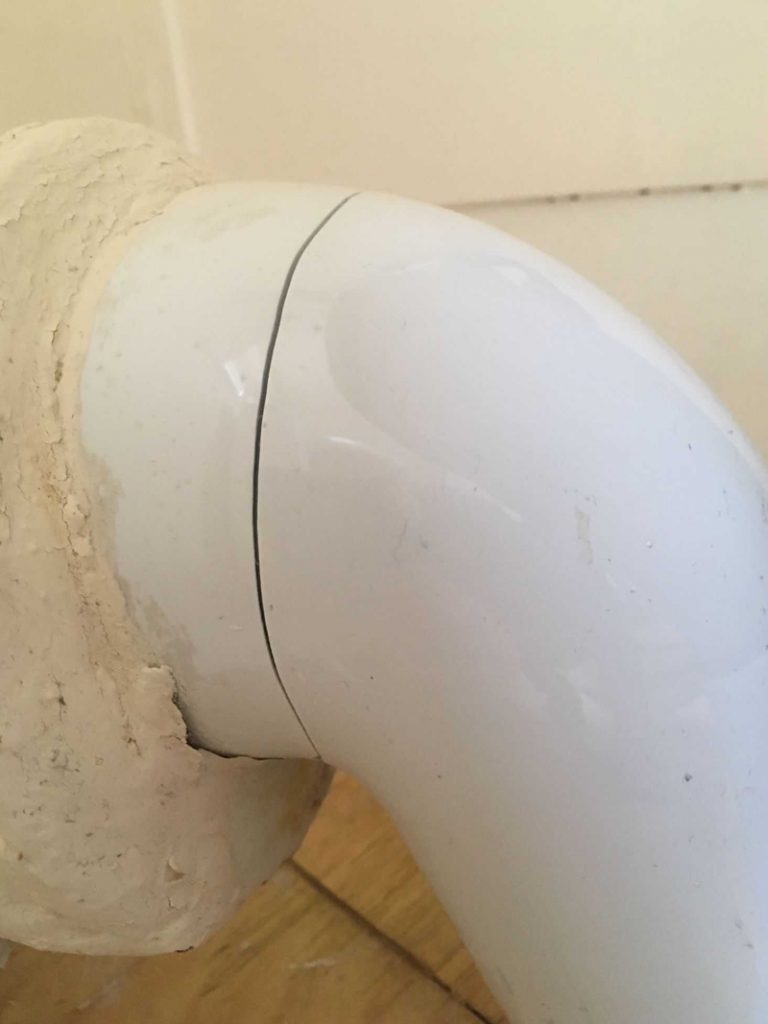 A hairline crack in a porcelain toilet waste pipe caused by an unstable floor