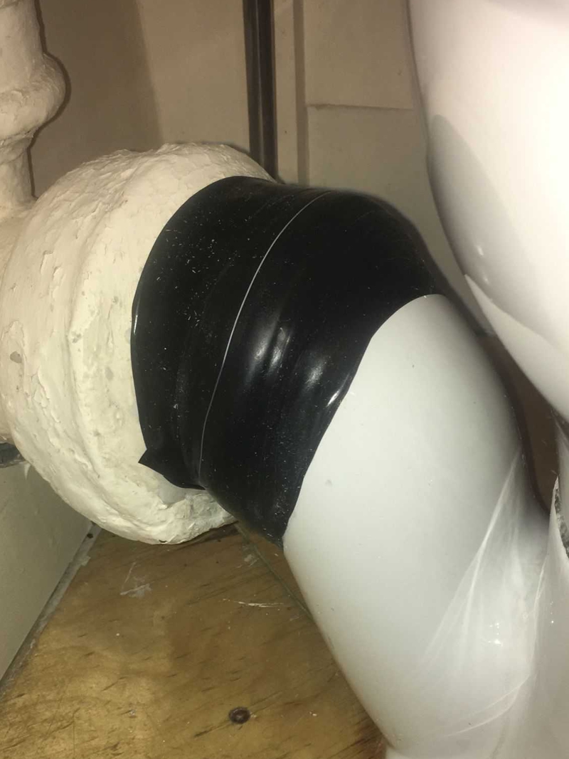 A hairline crack in a porcelain toilet soil pipe having undergone repair with Wrap & Seal Pipe Burst Tape 